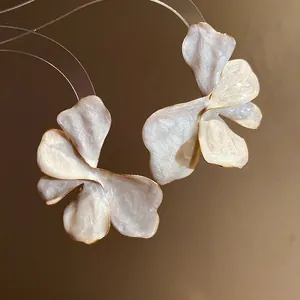 Detailed view of iridescent white enamel flower earrings with minimalist gold plating