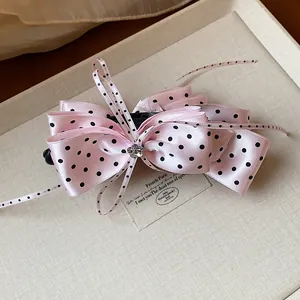 Vue détaillée d'une pince à cheveux élégante en satin rose à pois noirs sur un plateau beige