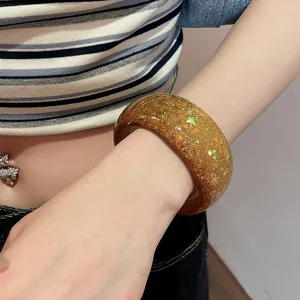 Detailed view of a chunky amber resin bangle with iridescent star sequins on wrist