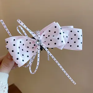 Détail d'une pince à cheveux à nœud rose à pois avec un centre en cœur de cristal