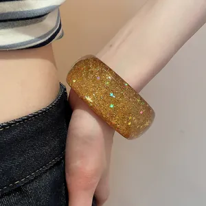 Close-up of a chunky golden resin bangle with glitter and star sequins on a wrist.
