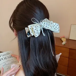 Gros plan d'une élégante barrette nœud blanche à pois noirs dans des cheveux longs.