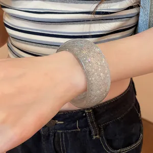Detail view of a clear resin bangle with sparkling silver sequins worn on a wrist.