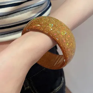 Close-up of an amber resin bangle featuring gold glitter and star sequins.