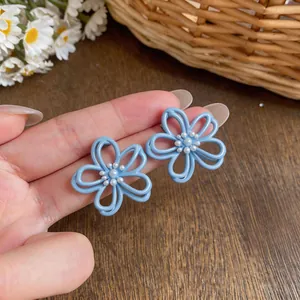 Primo piano di orecchini a fiore blu traforati con perle centrali, gioielli chic
