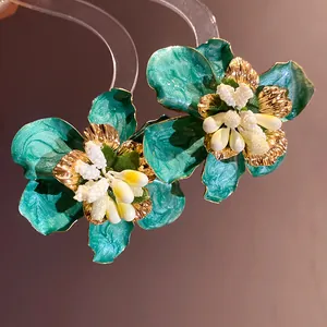 Dettaglio di orecchini a lobo a fiore boho verde acqua con bordi dorati e smalto