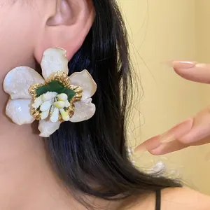Dettaglio ravvicinato di un grande orecchino a fiore bianco con bordi dorati su un orecchio.
