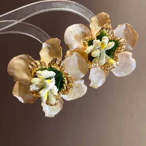 Dettaglio orecchini a lobo a forma di fiore in smalto crema stile boho dorato