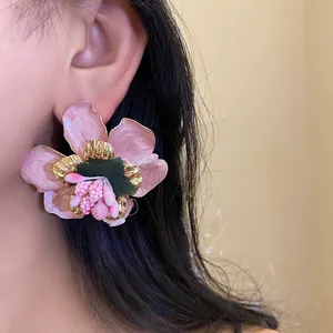 Dettaglio di orecchino a fiore in smalto rosa con bordi dorati in stile bohémien.