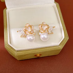 Primer plano de elegantes pendientes de perlas y flores con circonita en una caja verde.