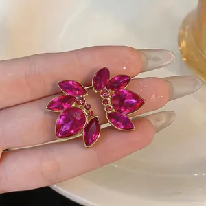 Dettaglio degli orecchini a foglia con cristalli fucsia tenuti su una mano.
