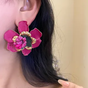 Dettaglio di un vivace orecchino a fiore fucsia con bordi dorati indossato da una modella
