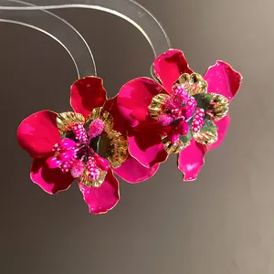 Vista macro di orecchini a fiore in smalto fucsia con stami dorati su sfondo scuro