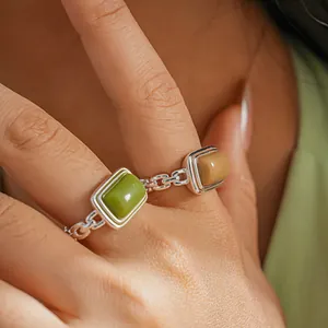 Close-up view of a stylish silver chain ring featuring green and yellow rectangular resin stones.