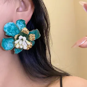 Dettaglio ravvicinato di un grande orecchino a fiore in smalto color verde acqua su una modella