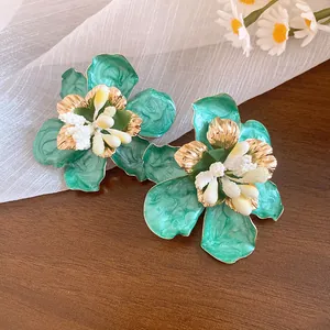 Dettaglio macro di orecchini a fiore in smalto verde con accenti dorati in stile boho
