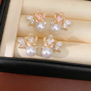 Detalle de elegantes pendientes de flor esmaltada rosa y perlas con detalles de circón