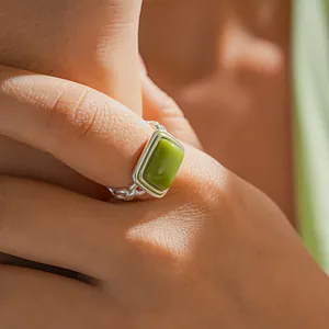 Close-up of a green square resin ring with a silver chain-link band on a finger.