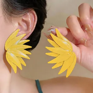 Close-up of yellow leaf-shaped stud earrings with detailed texture shown on a model's ear
