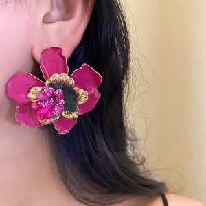 Dettaglio di orecchino a fiore in smalto rosa con bordi dorati per stile boho beach