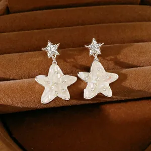 Vista dettagliata di orecchini a stella con inserto in conchiglia e strass su velluto marrone.