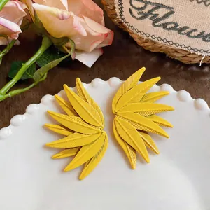 Close-up of vibrant yellow leaf-textured stud earrings displayed on a white beaded plate