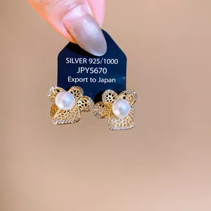 Close-up detail of gold-tone hollow flower earrings accented with white pearl and zircon