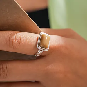 Close-up of a silver ring with a rectangular tan resin stone on an index finger