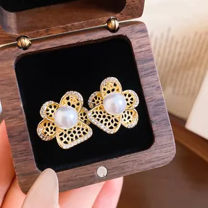 Detailed view of gold-tone hollow flower earrings with central pearl and zircons.