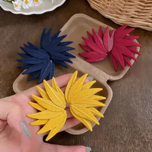 Close-up of exaggerated leaf texture earrings in yellow, blue, and burgundy colors.