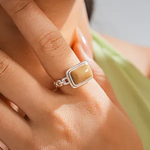 Detail shot of a rectangular tan resin ring with a silver chain-link band on a finger