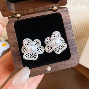 Close-up of elegant hollow flower earrings with pearls and zircons in a wooden jewelry box.