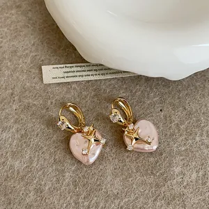Macro view showing pink heart-shaped pearl earrings with a gold star and zircon detail