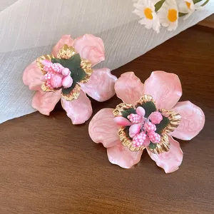 Dettaglio degli orecchini a fiore rosa con trama dorata e stami di perline.