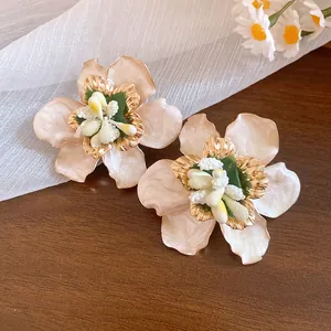 Dettaglio di orecchini floreali in stile boho con finitura smaltata su sfondo di legno