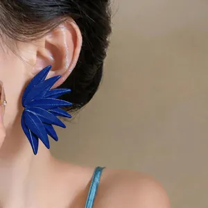 Close-up detail of oversized dark blue leaf-textured earring on a female model