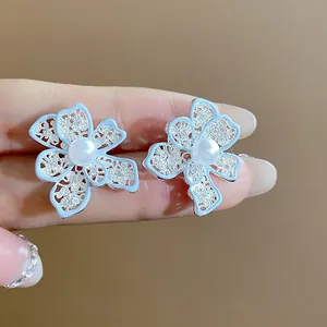 Dettaglio di orecchini a fiore con perle, smalto azzurro e pietre brillanti incastonate.