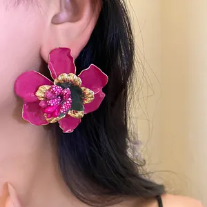 Primo piano di orecchini floreali in smalto rosa vibrante indossati da una modella