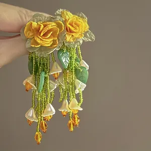 Close-up of handmade yellow chiffon flower earrings with long green bead tassels.