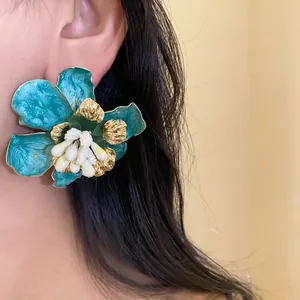 Primo piano di un grande orecchino a fiore in smalto verde acqua con petali dorati.
