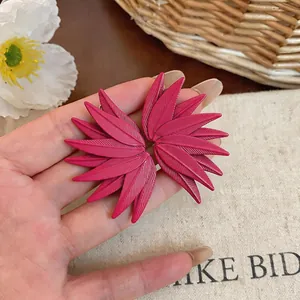 Close-up macro view of vibrant fuchsia leaf texture stud earrings held in hand