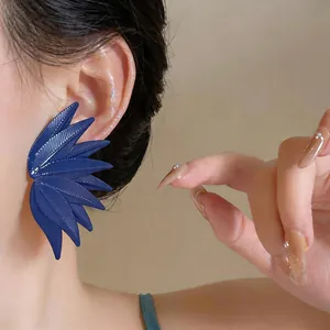 Close-up detail of oversized navy blue leaf texture stud earring worn by a model in beige setting.