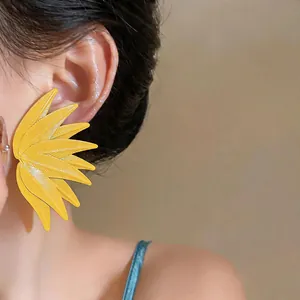 Close-up of vibrant yellow leaf-patterned earrings worn on a model's ear