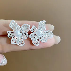 Dettaglio di orecchini a lobo a forma di fiore smaltato bianco con perla centrale.