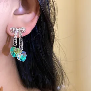 Close-up of iridescent heart crystal bow earrings worn on a model ear, detailed view