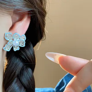 Primo piano dettagliato di orecchino a fiore cavo azzurro con perla sull'orecchio