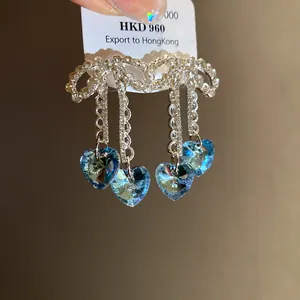 Close-up of sparkling zircon bow earrings with dangling blue heart shape crystals.