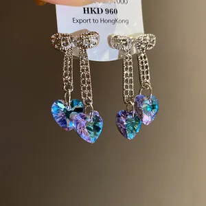 Close-up detail of silver bow earrings featuring iridescent heart-shaped zircon pendants