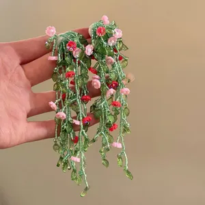 Handheld detail of long green beaded tassel earrings with pink flower charms