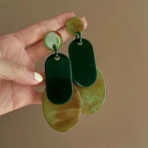 Detail view of large green and marbled acrylic geometric drop earrings held by hand.